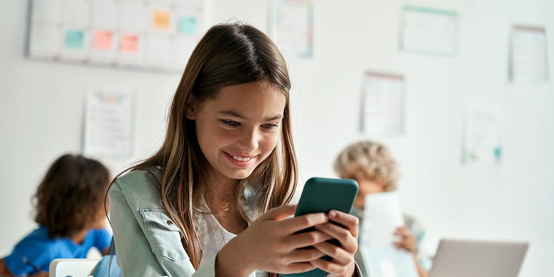 Mädchen in der Schule schaut auf sein Smartphone und lacht