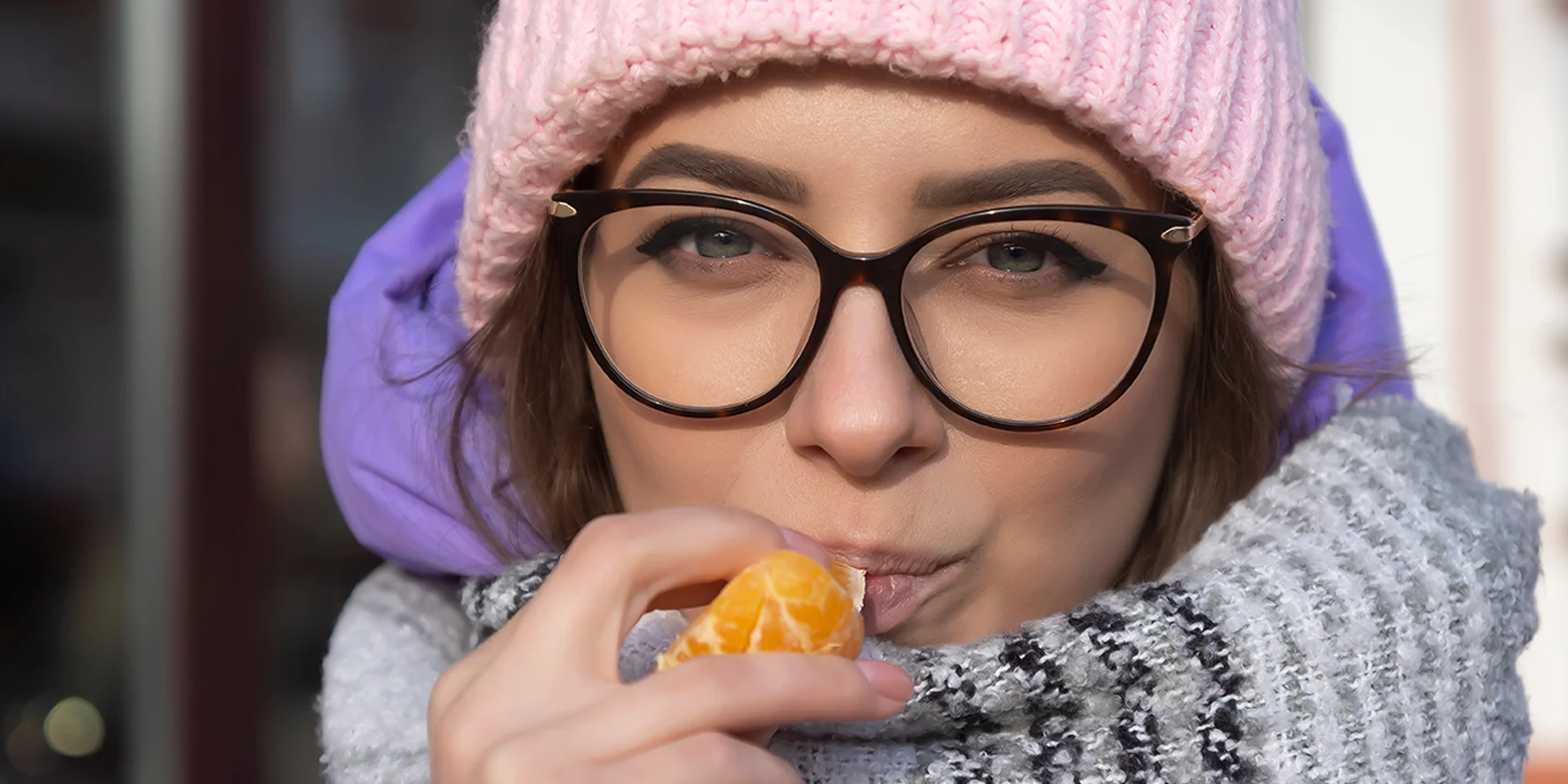 Frau mit Mütze und Schal isst eine Orange